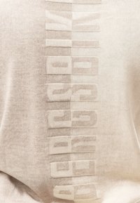 Tessuto beige morbido con il testo rialzato "ARMANI EXCHANGE" embossato al centro in verticale.