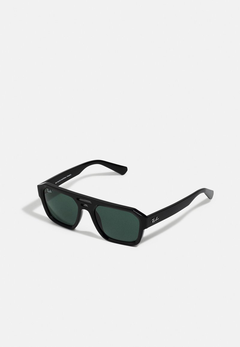 Melni taisnstūra saulesbrilles ar zaļiem stikliem. Izgatavotas no plastmasas ar oktagonālu formu un gludu apdari. Sānos redzama Ray-Ban zīmola nosaukums.