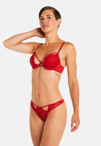 Ensemble de lingerie en dentelle rouge comprenant un soutien-gorge rembourré avec des détails brodés et un string assorti. Design à lanières avec des découpes accentuées.