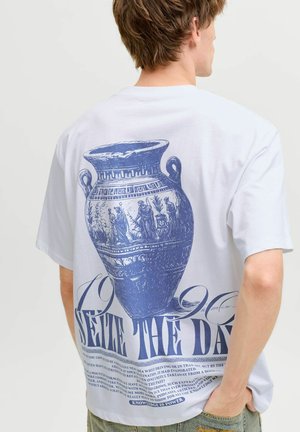Person trägt ein weißes T-Shirt mit einer großen blauen Illustration einer antiken griechischen Vase und dem Text „Seize the Day“ auf der Rückseite.