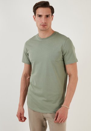 Tricou scurt, de culoare verde măsliniu, confecționat dintr-un material moale, cu guler rotund. Modelul stă pe un fundal neutru, cu mâinile pe lângă corp.