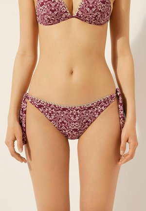 Bikini d'un rouge bourgogne foncé avec des motifs floraux complexes ; haut triangulaire avec bretelles réglables, et bas de bikini à nouer sur les côtés avec une finition en dentelle.
