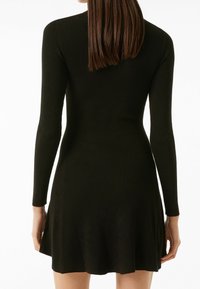 Robe noire à manches longues en tissu côtelé avec une jupe évasée, dotée d'un corsage ajusté et d'un tissu texturé, offrant une apparence douce et lisse.