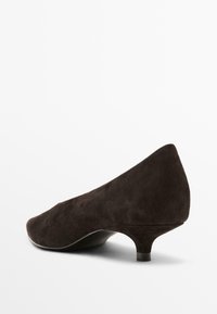 Bruine suède pump met een spitse neus en een kleine, taps toelopende hak. Beschikt over een gladde textuur en een strakke, minimalistische uitstraling.