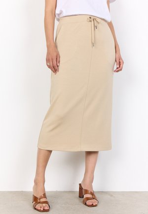 Beige, knee-length skirt made from soft fabric with an elastic waistband and drawstring. Smooth texture and simple design, paired with brown heeled sandals.
