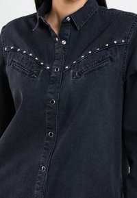 Black denim shirt with snap buttons, featuring rounded pockets and studded accents across the chest and shoulders. Soft texture.
