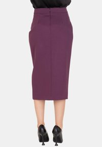 Gonna a matita viola con design aderente, taglio al ginocchio, chiusura con cerniera posteriore e due tasche posteriori. Indossata con scarpe nere con tacco.
