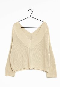 Beżowy sweter z dzianiny o głębokim dekolcie w kształcie litery V i prążkowanej fakturze, z krojem cropped i długimi rękawami, wiszący na czarnym wieszaku.