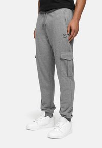 Pantalons cargo en coton gris avec taille élastique, cordon de serrage ajustable, poches latérales et poignets côtelés. Assortis à des baskets blanches.