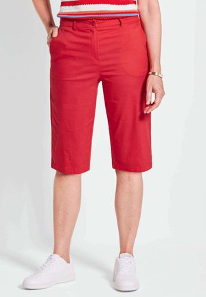 Shorts en bermuda rouges en tissu léger, avec une coupe droite, deux poches latérales et une fermeture à bouton. Assortis avec des baskets blanches.