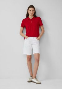 Rode polo met kraag, witte opgerolde shorts en beige sneakers met witte accenten. Eenvoudig ontwerp met een casual uitstraling.