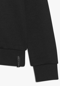 Czarny sweatshirt z prążkowanymi mankietami i dolnym wykończeniem, wykonany z teksturowanej tkaniny. Zawiera małą metkę z logo "Scotch & Soda".