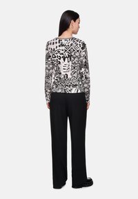 Long-sleeve top featuring a black and white graphic print with various patterns, paired with tailored black trousers and chunky black shoes.