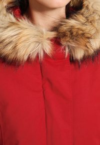 Rød parka-jakke med krave i kunstpels i nuancer af beige og brun. Har lynlåslukning og blødt, struktureret stof.