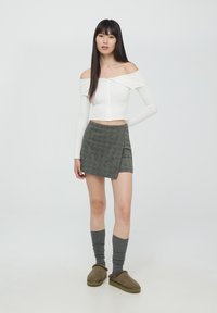 Biała bluzka z odkrytymi ramionami, szara spódnica w kratę z wykrojem, szare podkolanówki i brązowe buty typu slip-on, prezentujące warstwowy, minimalistyczny wygląd.