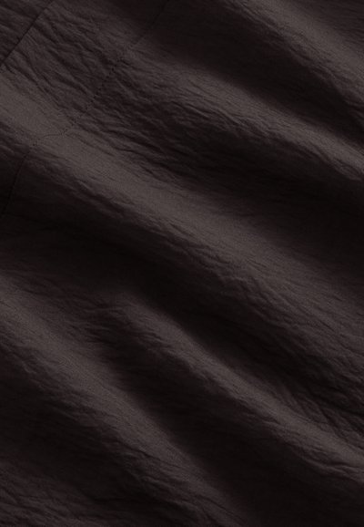 Tissu brun foncé avec des coutures diagonales visibles et des plis doux et irréguliers créant une surface texturée.