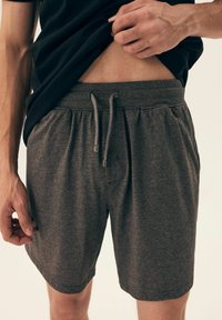 Szare spodenki sportowe z elastycznym pasem i regulowanym sznurkiem, posiadające boczne kieszenie oraz miękką teksturę, pokazane nad czarną koszulą.