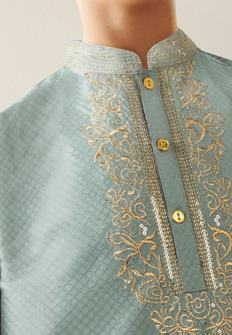 Gros plan sur un vêtement traditionnel bleu clair avec une broderie florale dorée, des paillettes, et trois boutons jaunes le long du plastron avant.