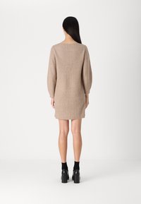Robe en tricot beige clair, avec une texture côtelée, des manches ballon et un dos creusé, dotée d'une jupe légèrement évasée. Des chaussures à plateforme noires sont portées.