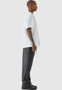 Hvit oversized t-skjorte, svarte joggebukser i kunstlær med glatt tekstur, og svarte joggesko, sett fra siden.