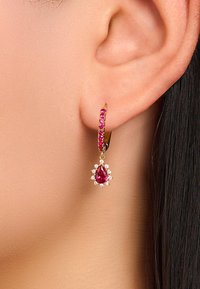 Goldene Creolenohrringe mit rosa Edelsteinen und einem tropfenförmigen Rubinanhänger, umgeben von kleinen klaren Steinen, heben die filigranen Details hervor.