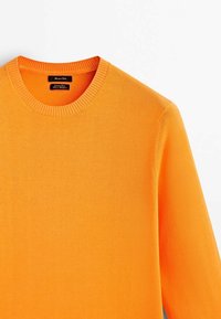 Pomarańczowy dziany sweter z okrągłym dekoltem. Posiada prążkowany kołnierz i mankiety, gładką teksturę oraz dopasowany krój. Metka widoczna wewnątrz kołnierza.