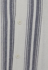 Tissu blanc avec des rayures verticales bleu marine et deux boutons blancs sur le devant texturé d'une chemise tissée.
