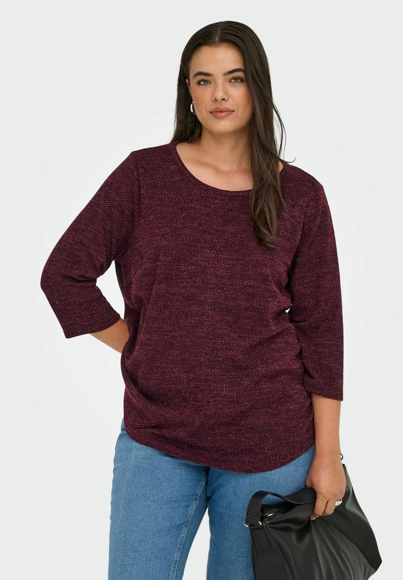 Top bordeaux con texture, maniche a tre quarti, scollatura rotonda e vestibilità ampia, abbinato a jeans blu chiaro e una borsa nera.