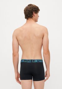 Zwarte boxershorts met een geblokt blauwe en groene tailleband met het "NIKE" logo. Het materiaal lijkt rekbaar en goed aansluitend.