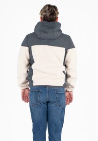 Felpa con parte superiore grigia e corpo in pile crema, dotata di cappuccio e polsini elastici, abbinata a jeans in denim blu.