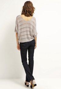 Pull en tricot lâche gris clair avec encolure dégagée et manches courtes, associé à un jean slim en denim foncé et des escarpins.