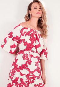Off-the-shoulder dress with white fabric featuring bold red floral patterns, flared sleeves, and an elastic waistband for a relaxed fit.