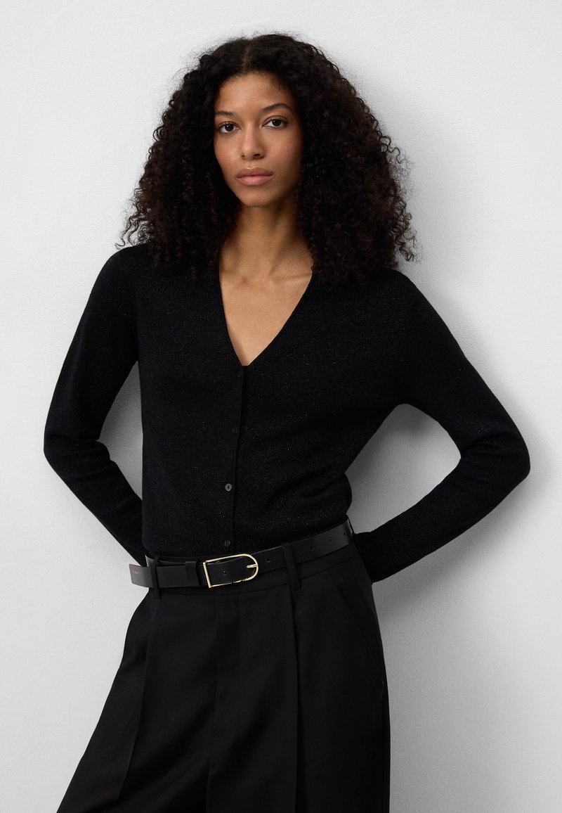 Zwarte cardigan met een V-hals, lange mouwen en subtiele glans. Knopen sluiting en een getailleerd ontwerp, gecombineerd met hoge taille broeken en een riem.