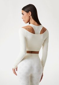 Top corto bianco a maniche lunghe con scollatura ampia e motivo testurizzato. Leggings aderenti abbinati con design in rilievo in una tonalità simile.