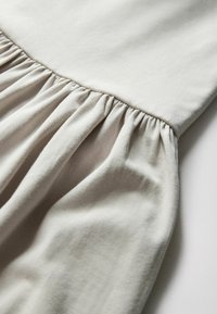 Tissu beige doux avec couture froncée créant des plis, montrant la texture et le drapé du matériau léger.