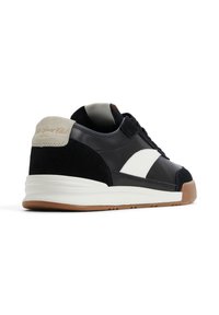 Zapatilla en blanco y negro con parte superior de cuero y gamuza, acento en el talón color crema y suela de goma. Diseño simplista.
