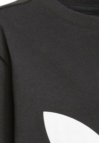 Črn material z rebrasto teksturo, ki ima veliko belo grafično zasnovo. Ovratnik je okrogel, kar poudarja minimalistični slog.