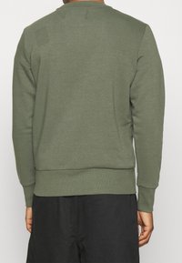Sudadera verde caqui con mangas largas, puños y dobladillo acanalados, tejido suave, cuello redondo y detalles mínimos en la parte trasera.