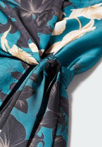 Bloemige stof met een turquoise achtergrond, met donkere bladeren en crèmekleurige bloemen. Het materiaal is soepel met een subtiele glans en valt mooi.