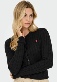 Cardigan nero a maglia con maniche lunghe, scollo rotondo e cinque bottoni, con un piccolo cuore rosso ricamato sul petto.