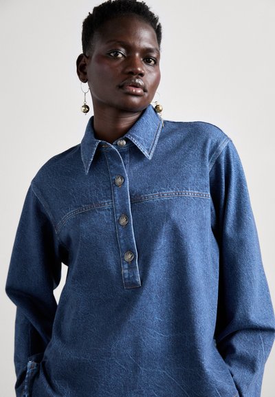 Denim shirt in dark blue with a buttoned collar, featuring a placket with three metallic buttons, and a textured fabric finish.