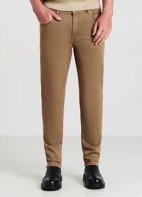 Braune Slim-Fit-Hosen mit glatter Textur, Fünf-Taschen-Design und sichtbaren Nähten, kombiniert mit schwarzen Ankle-Boots.