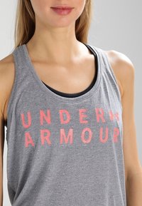 Szary bezrękawnik z napisem "UNDER ARMOUR" w wyrazistych różowych literach. Miękka tkanina z okrągłym dekoltem i warstwowym fasonem.