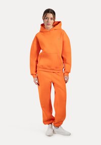Lys orange hoodie og sweatsæt i et blødt materiale. Hoodie har en frontlomme og ribbede manchetter; slim-fit bukser har elastiske ankler.