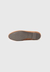 Brown suede shoe with a flat, textured rubber sole. Features a rounded toe and minimalistic design, emphasizing clean lines.
