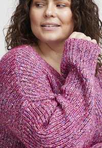 Texturerad stickad tröja i livlig pink med inslag av blått och grönt. Har en V-ringad hals och oversized passform som framhäver det mjuka tyget.