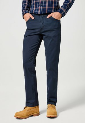 Chino blu navy con una texture liscia, dotati di tasche laterali e un design slim fit. Abbinati a stivali in suede marrone chiaro.