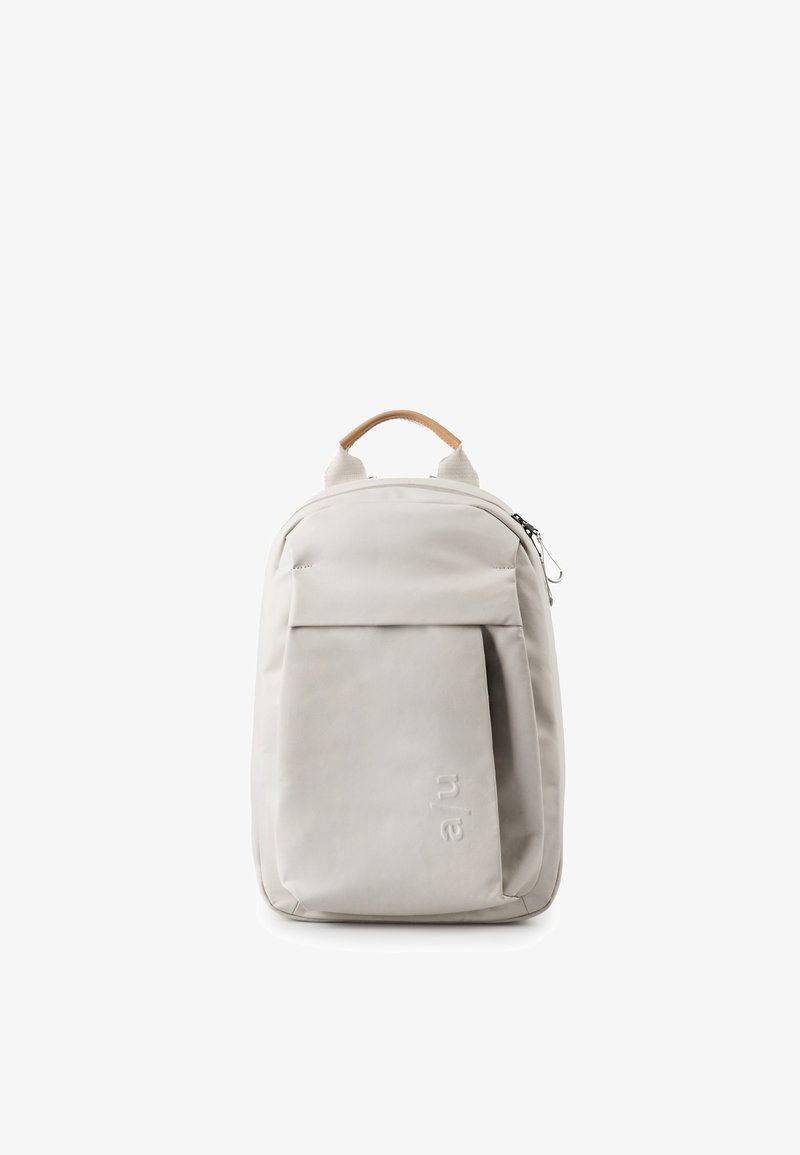 Zaino minimalista grigio chiaro con tasca anteriore a patta, manico color cuoio e chiusura con cerniera, mostrato su sfondo bianco.