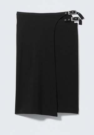 Jupe portefeuille noire avec deux bretelles argentées à boucles sur le côté droit, présentant une coupe droite et une longueur au genou.