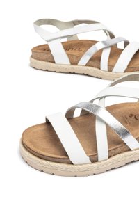 White and metallic silver sandals with multiple crossed straps, soft brown insole, and woven jute bottom, featuring a textured rubber sole.
